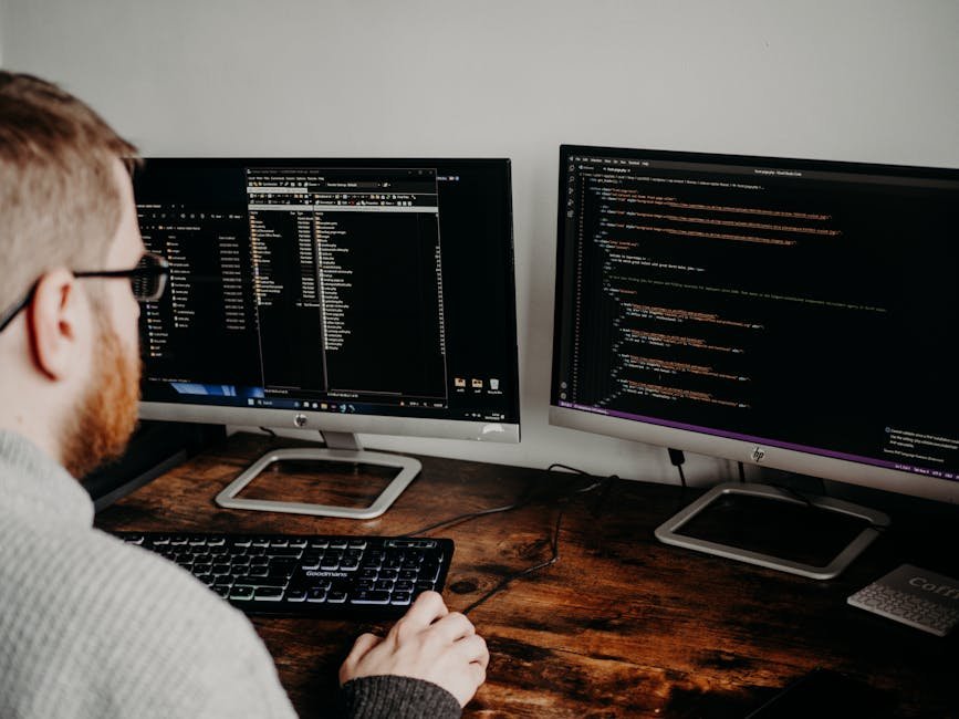 Software developer working on code with dual monitors in a home office setting.