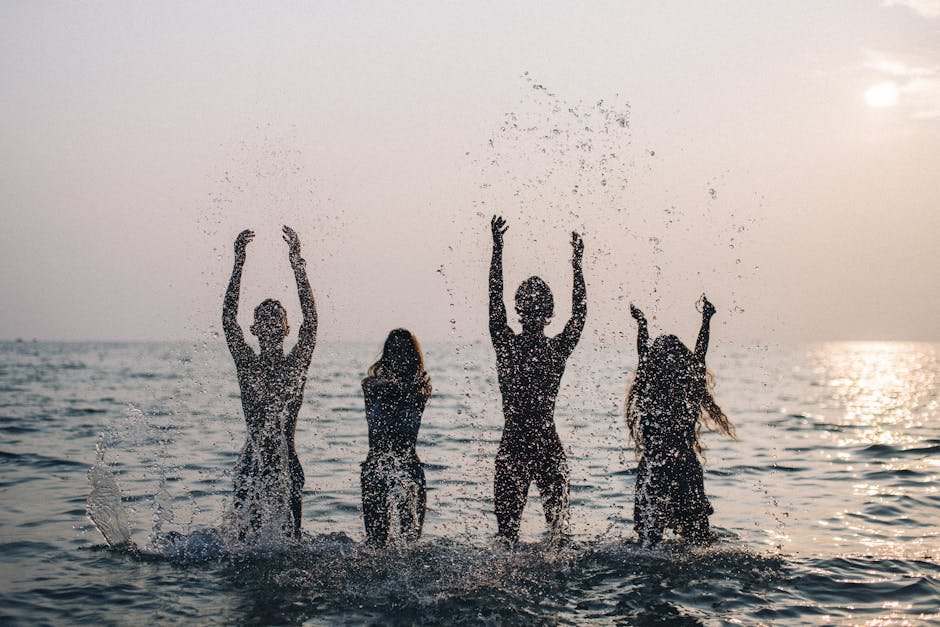 Silhouettes of four people joyfully splashing water in the sea during a beautiful sunset.